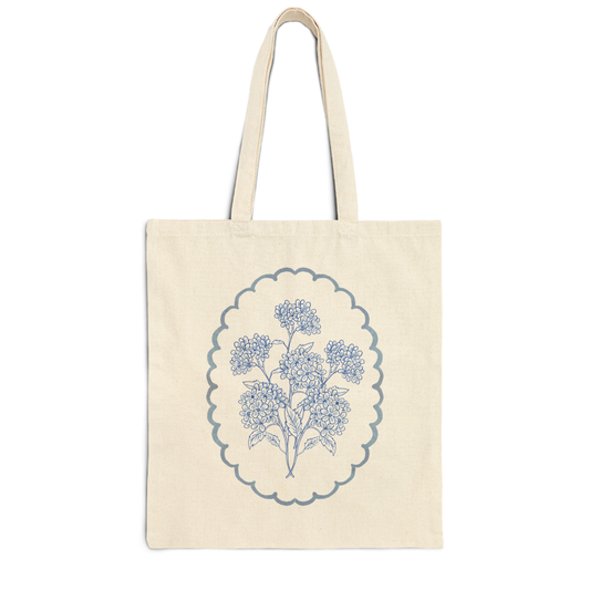 Natural canvas tote bag featuring a blue hydrangea floral illustration inside a scalloped frame