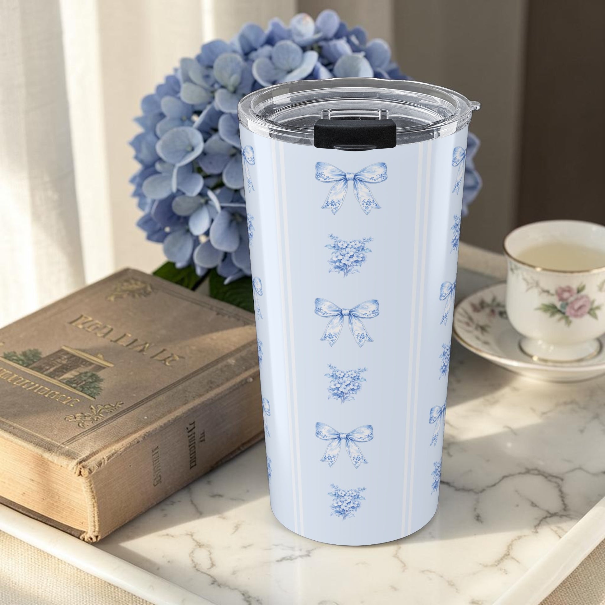 20 oz blue hydrangea and bow tumbler styled with vintage books and hydrangea flowers in a cozy reading nook scene