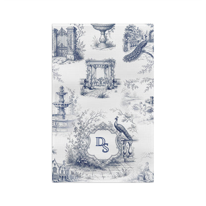 Front view of a personalized blue toile tea towel with estate garden scenes, peacocks, swans, and a custom monogram frame.
