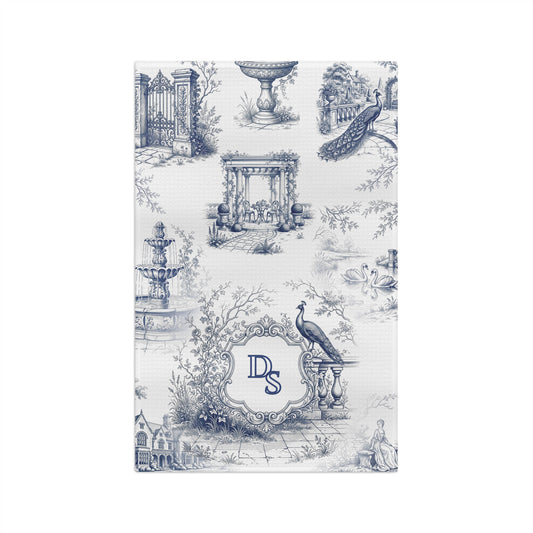 Front view of a personalized blue toile tea towel with estate garden scenes, peacocks, swans, and a custom monogram frame.