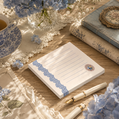 Lined vintage floral sticky note pad displayed with elegant stationery, antique books, and blue hydrangeas in a warm cottagecore setting.